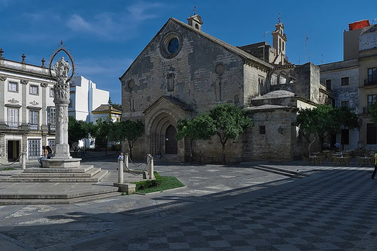 En brolagt plads i Jerez' gamle bydel med en gotisk stenkirke og en høj søjle foran en palæfacade