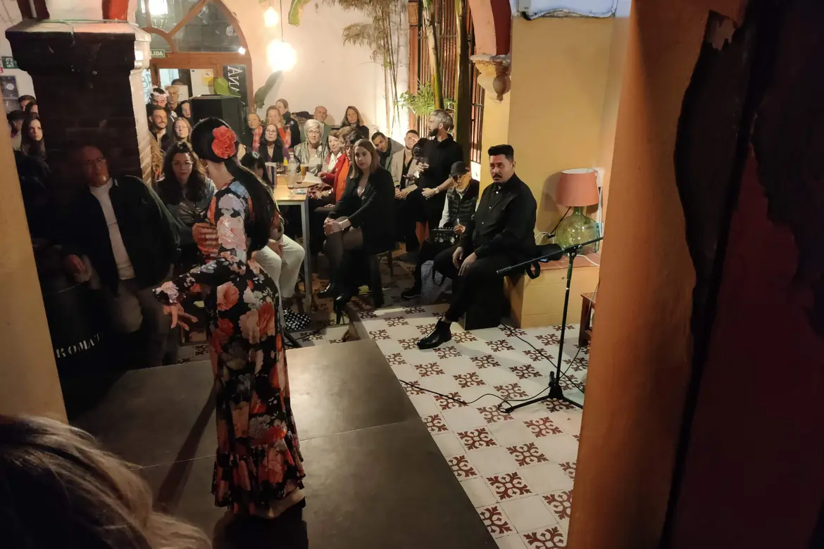 Una ballerina in abito fiorato si esibisce su un piccolo palco mentre il pubblico affollato del patio osserva dai tavoli